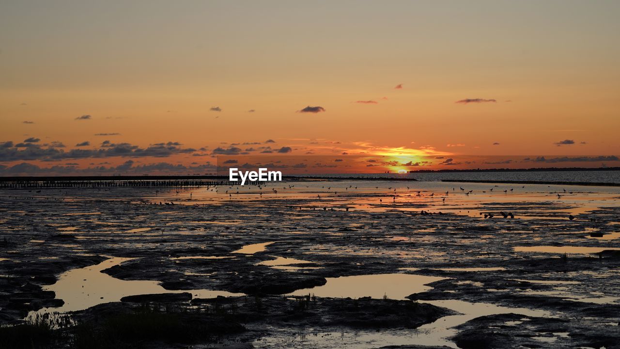 Scenic view of low tide at sea against sky during sunset
