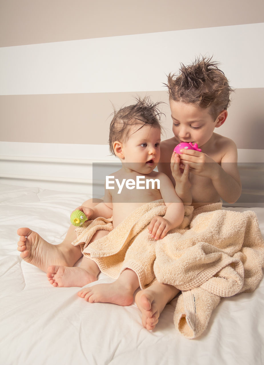 Cute shirtless siblings wrapped in towel against wall