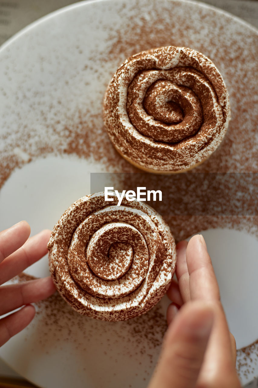 hand, food and drink, food, sweet food, one person, baked, holding, sweet, dessert, icing, indoors, cake, freshness, dish, close-up, adult, lifestyles, women, high angle view, temptation, finger, snack, personal perspective, produce, domestic room, cookie, cinnamon roll, swirl