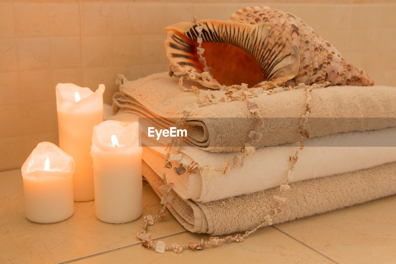Close-up of lit candles by towels and seashells in bathroom
