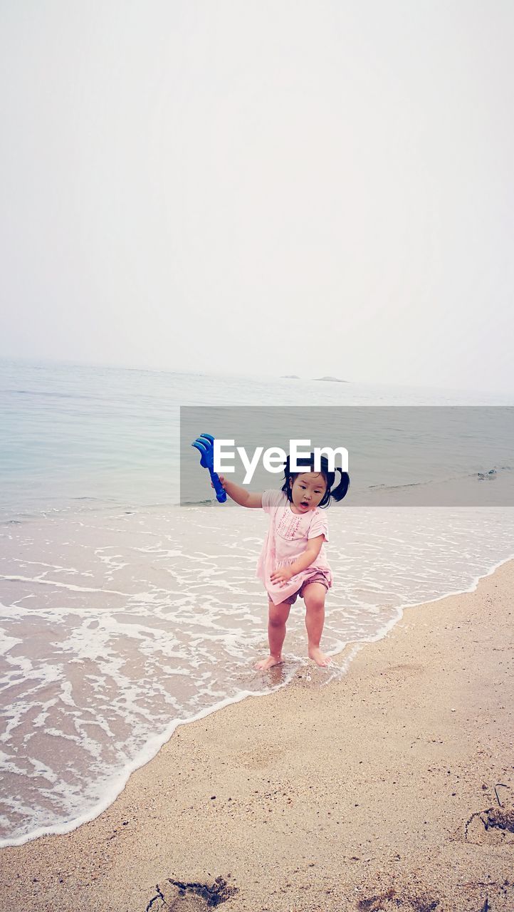 Girl holding toy rake while running on shore at beach against sky