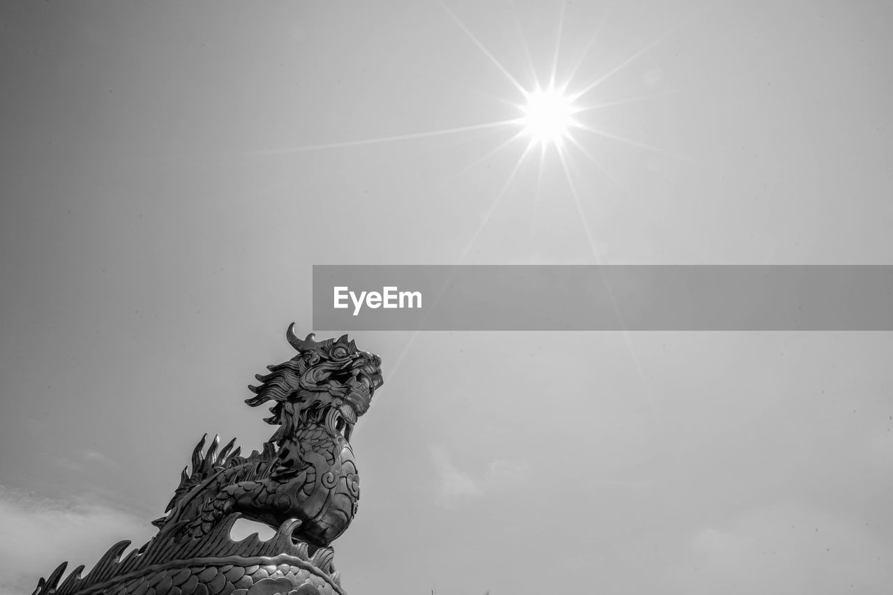 Low angle view of dragon statue against blue sky on sunny day