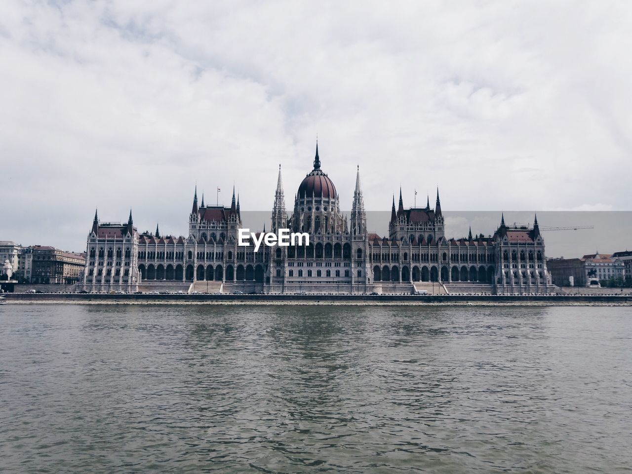 Hungarian parliament building by river against cloudy sky