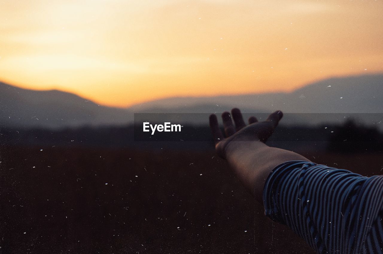 Cropped hand gesturing against sky during sunset