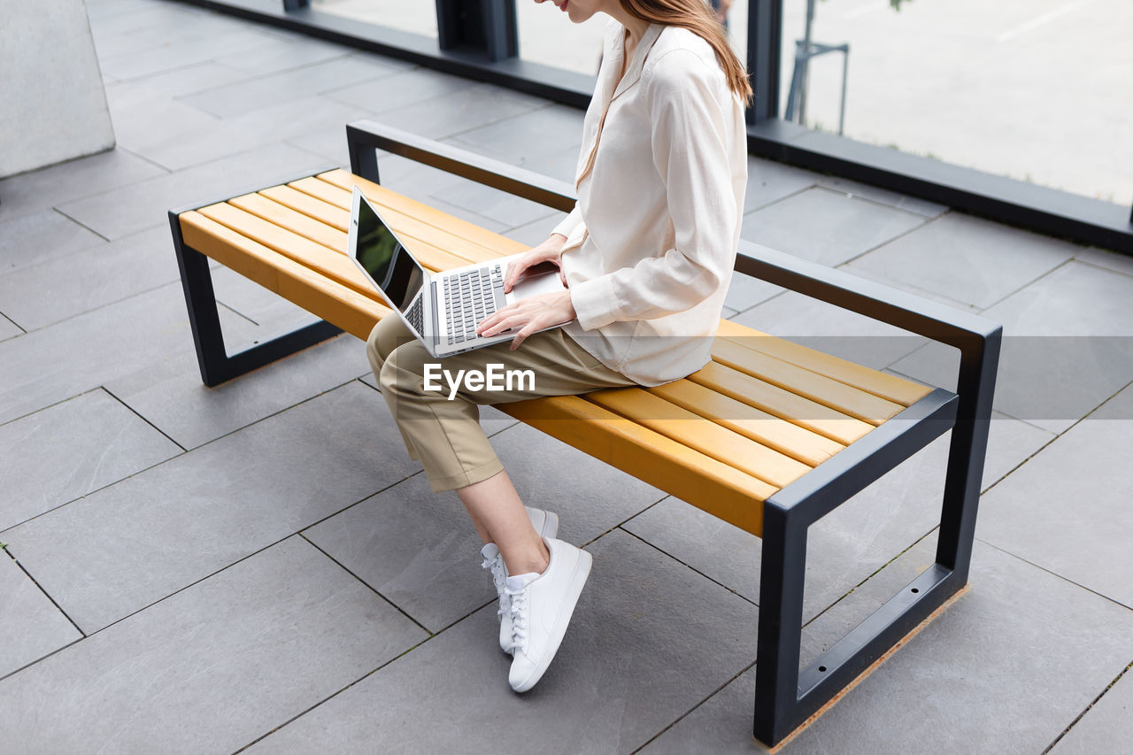 Young woman holding laptop and smartphone sitting on a bench