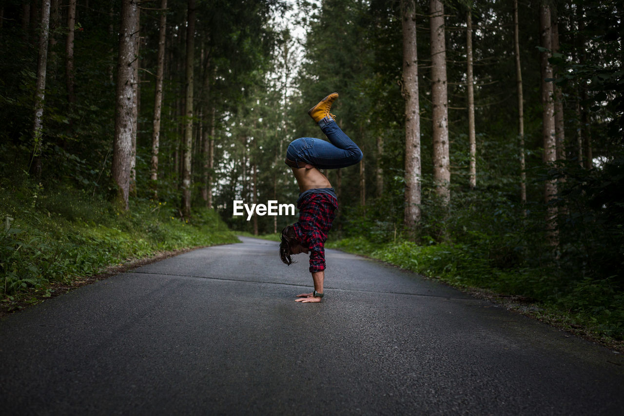 Full length side view of man doing handstand on road amidst forest