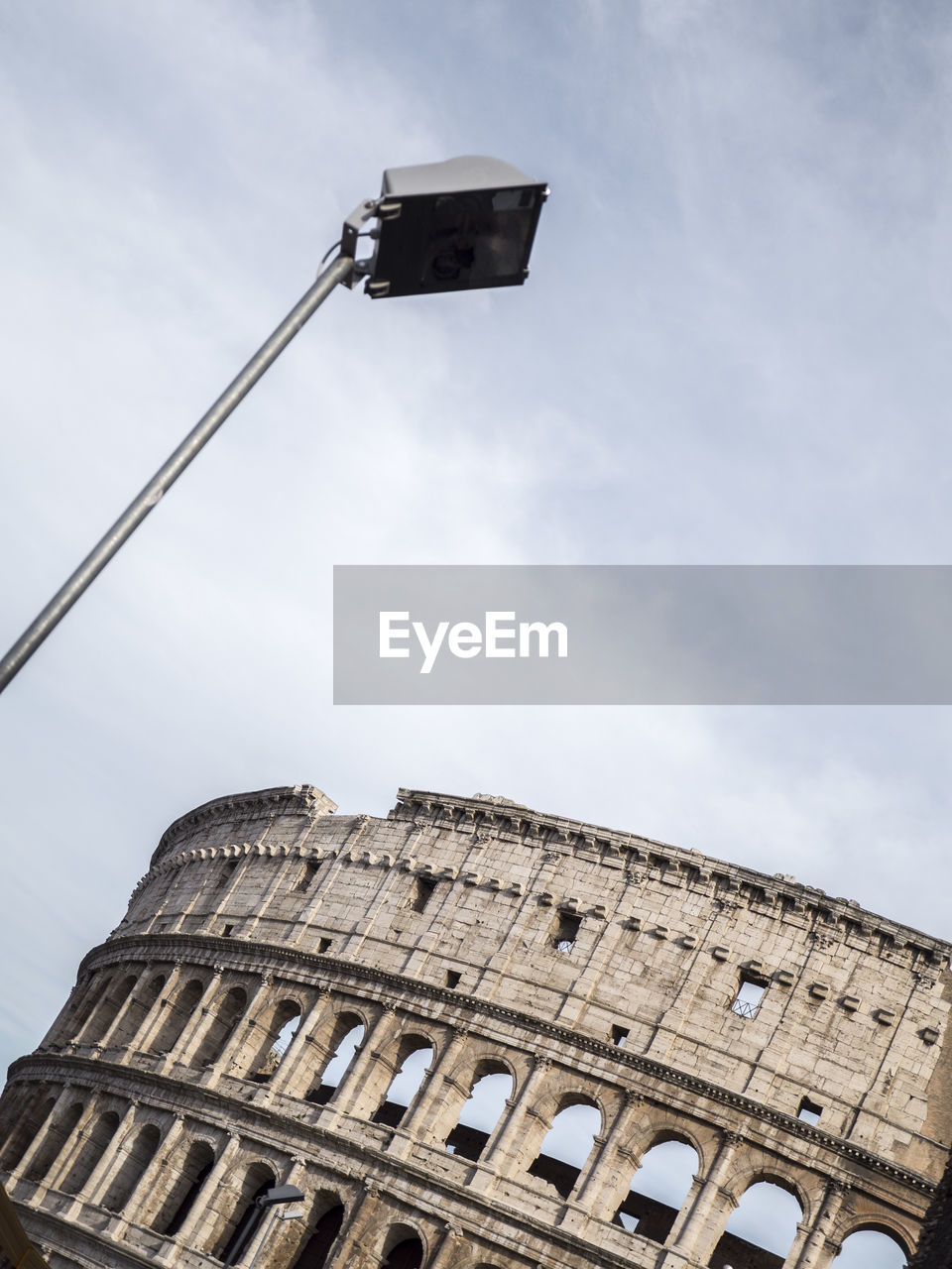 Low angle view of coliseum against cloudy sky