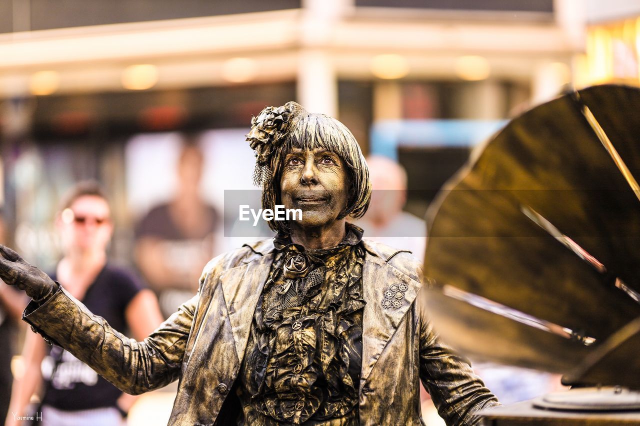 STATUE OF WOMAN WITH SCULPTURE IN BACKGROUND