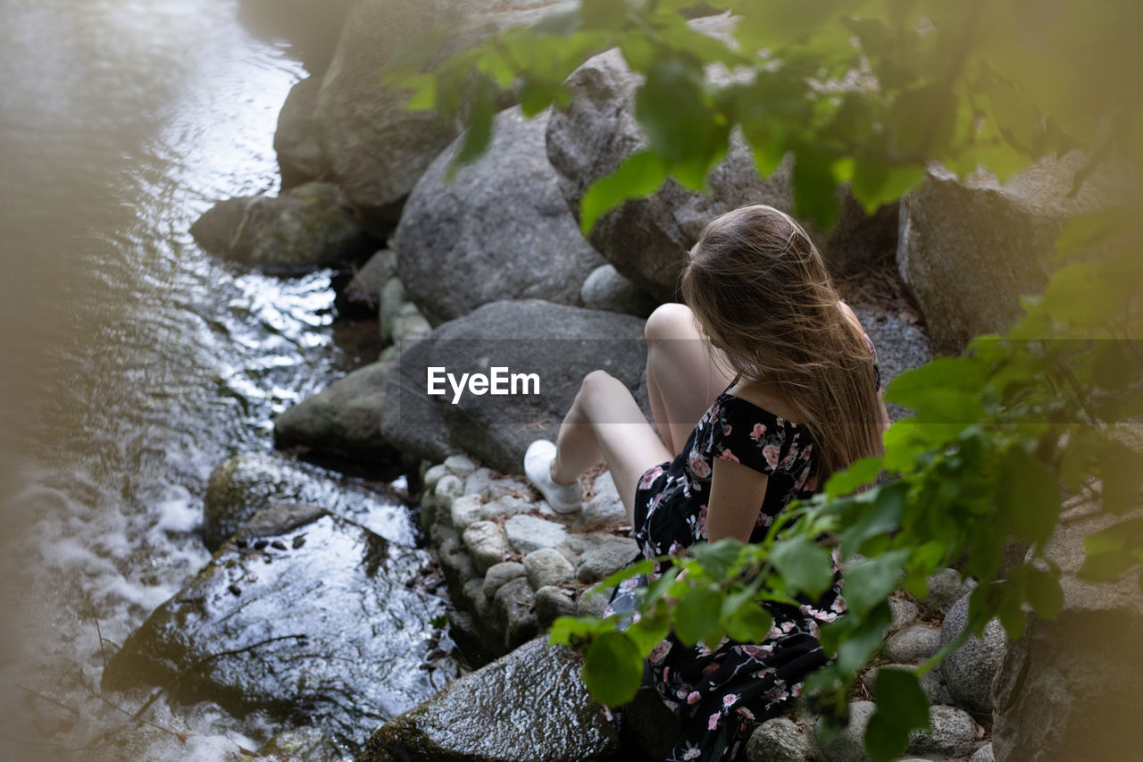 HIGH ANGLE VIEW OF WOMAN SITTING BY ROCKS