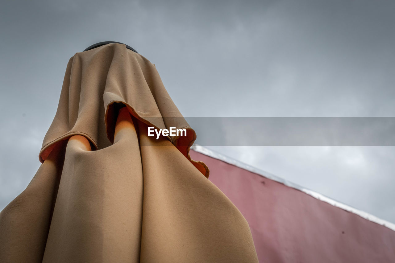 High section of folded parasol against cloudy sky