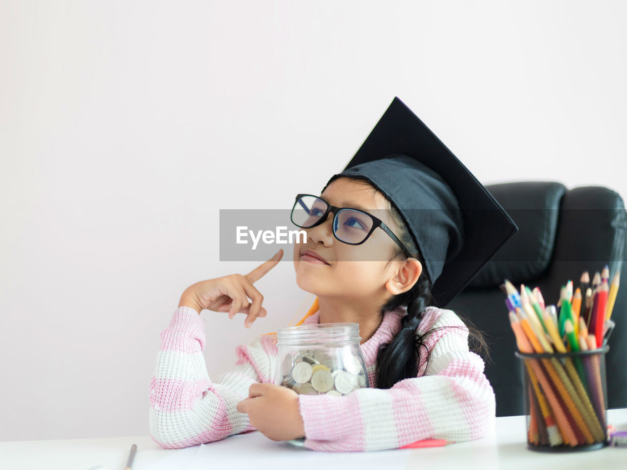 Smiling girl looking away while holding coins in jar on table