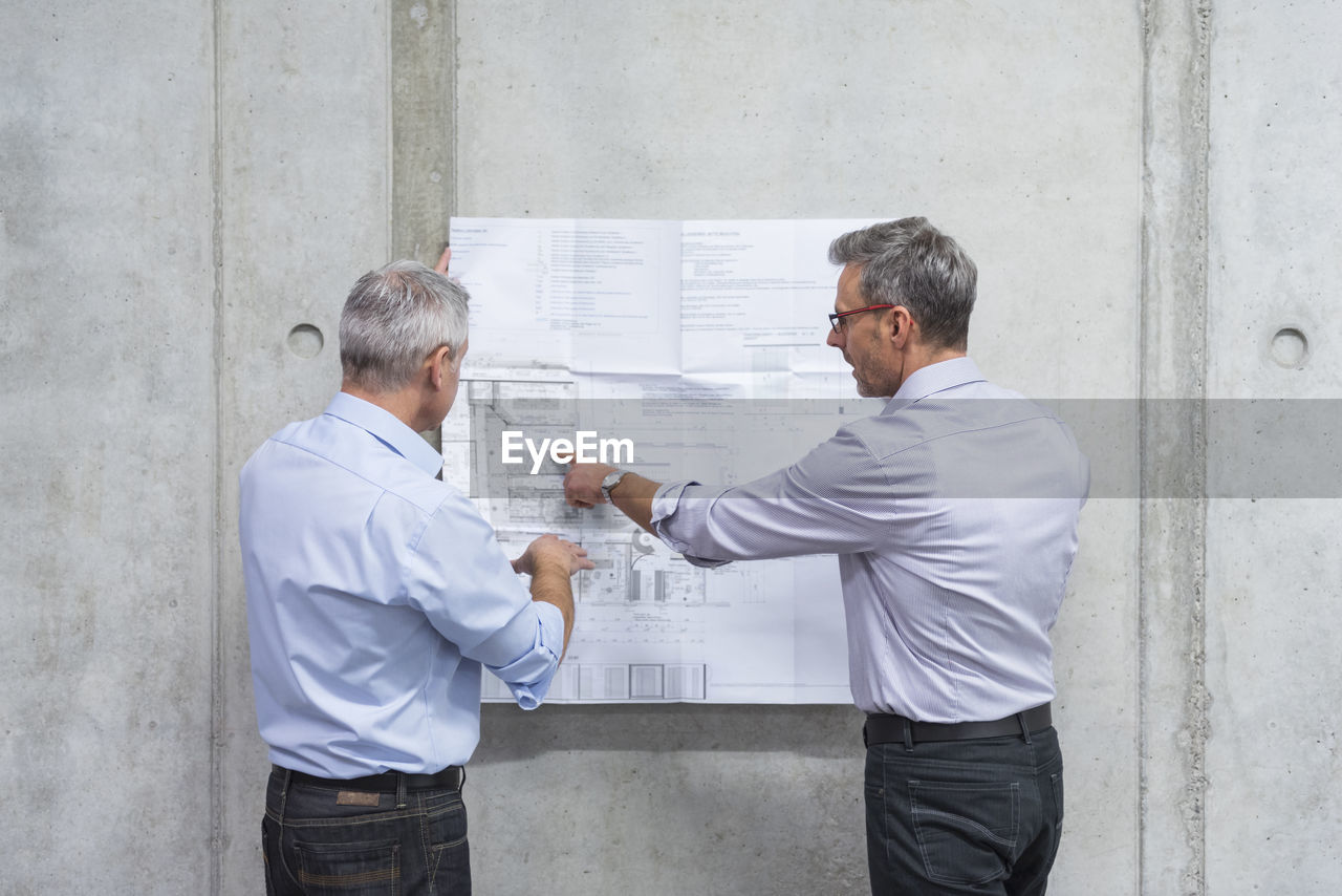 Two businessmen discussing construction plan at concrete wall