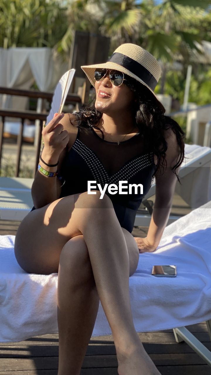 Beautiful woman wearing sunglasses and hat sitting outdoors