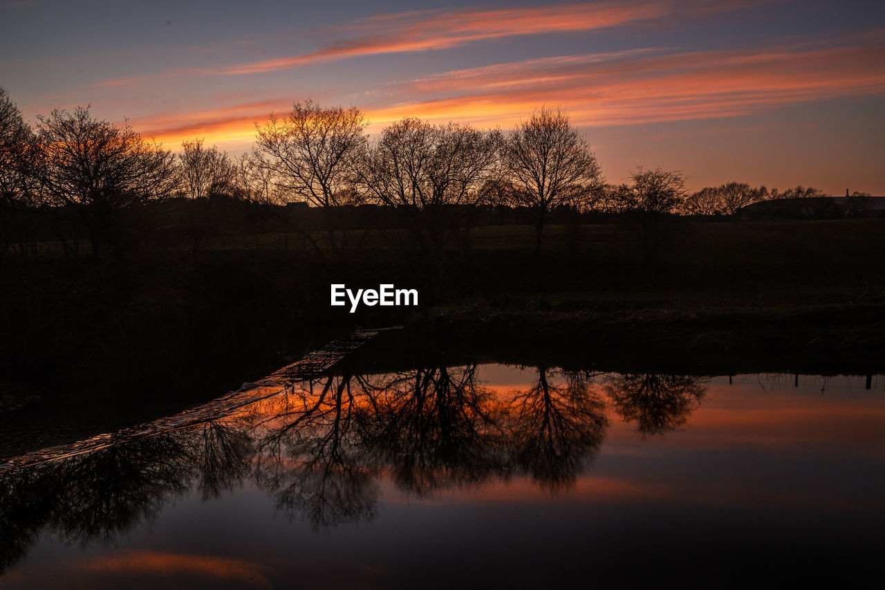 Silhouette trees by lake against sky during sunset