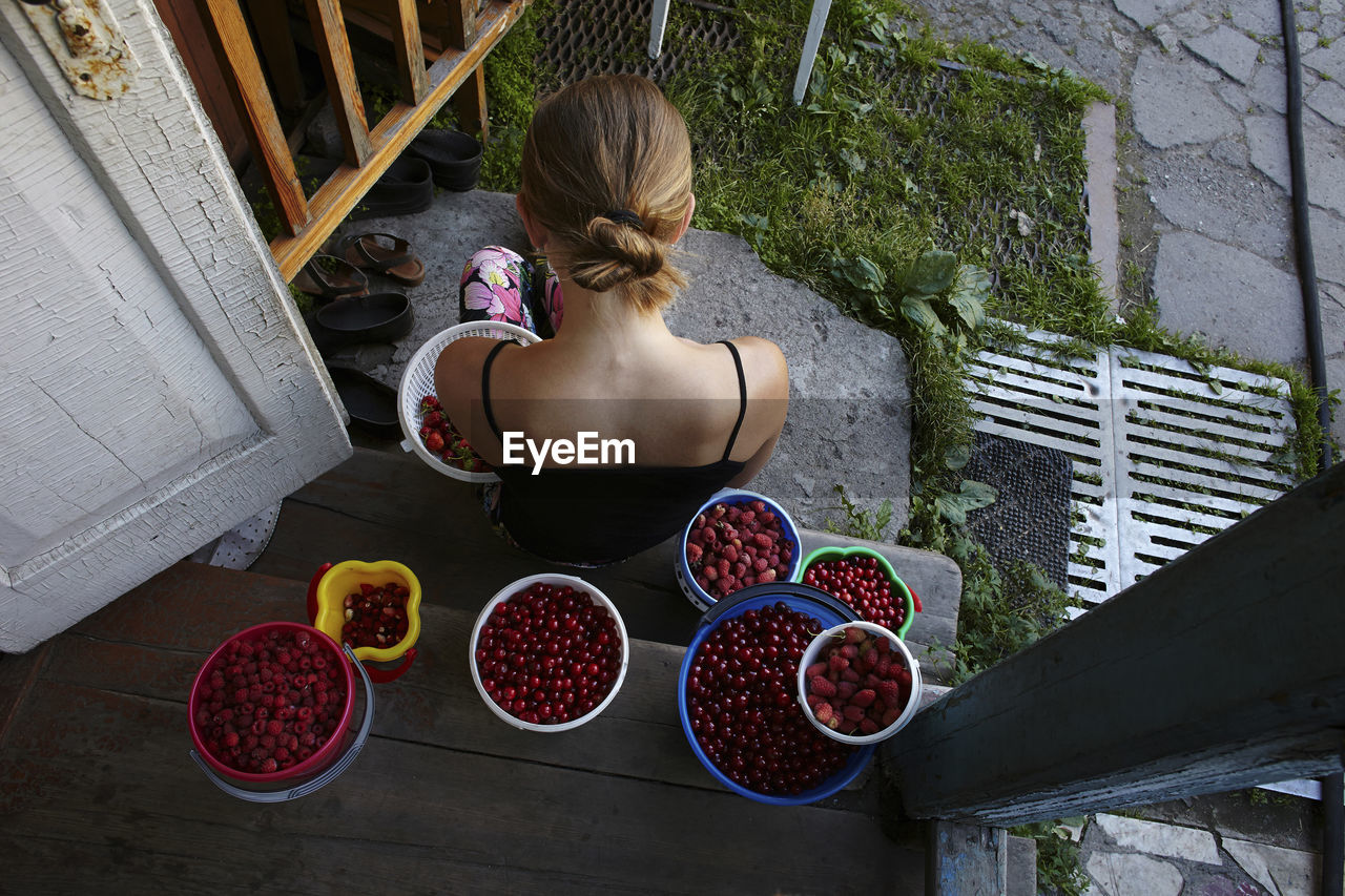 High angle view of woman with fruits in containers sitting at doorway
