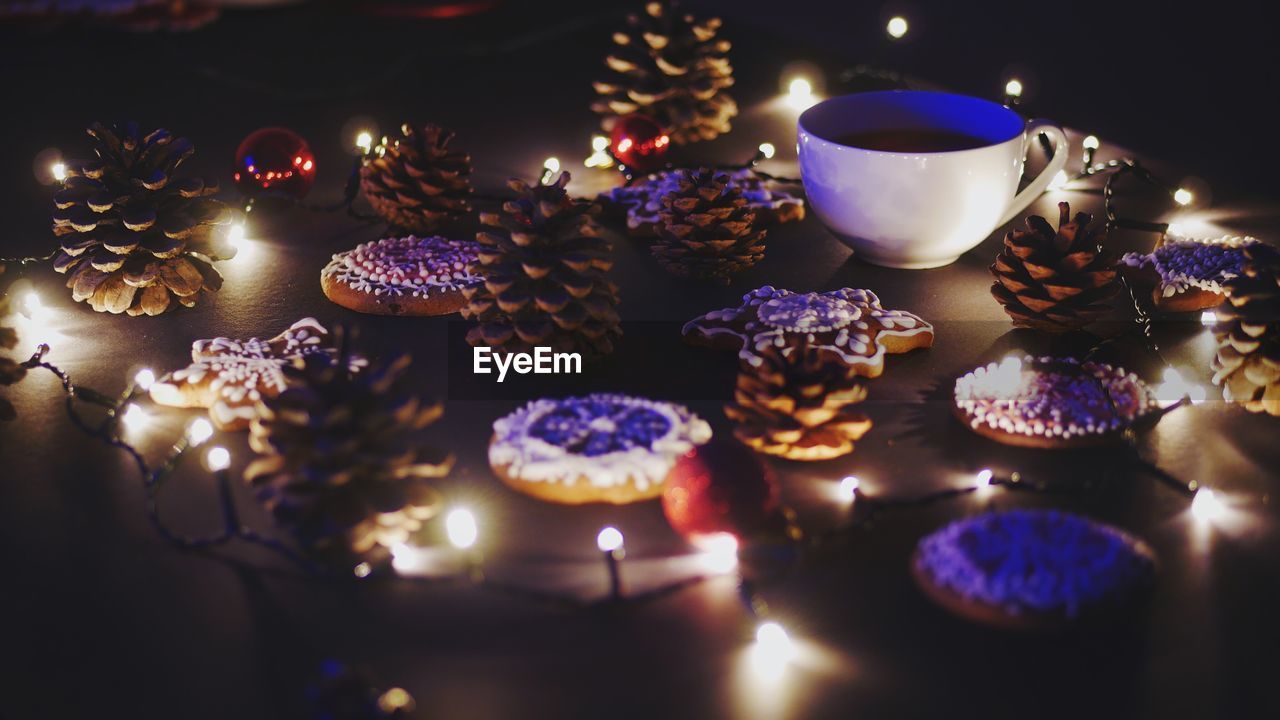 Close-up of coffee cup and gingerbread cookies amidst illuminated christmas lights