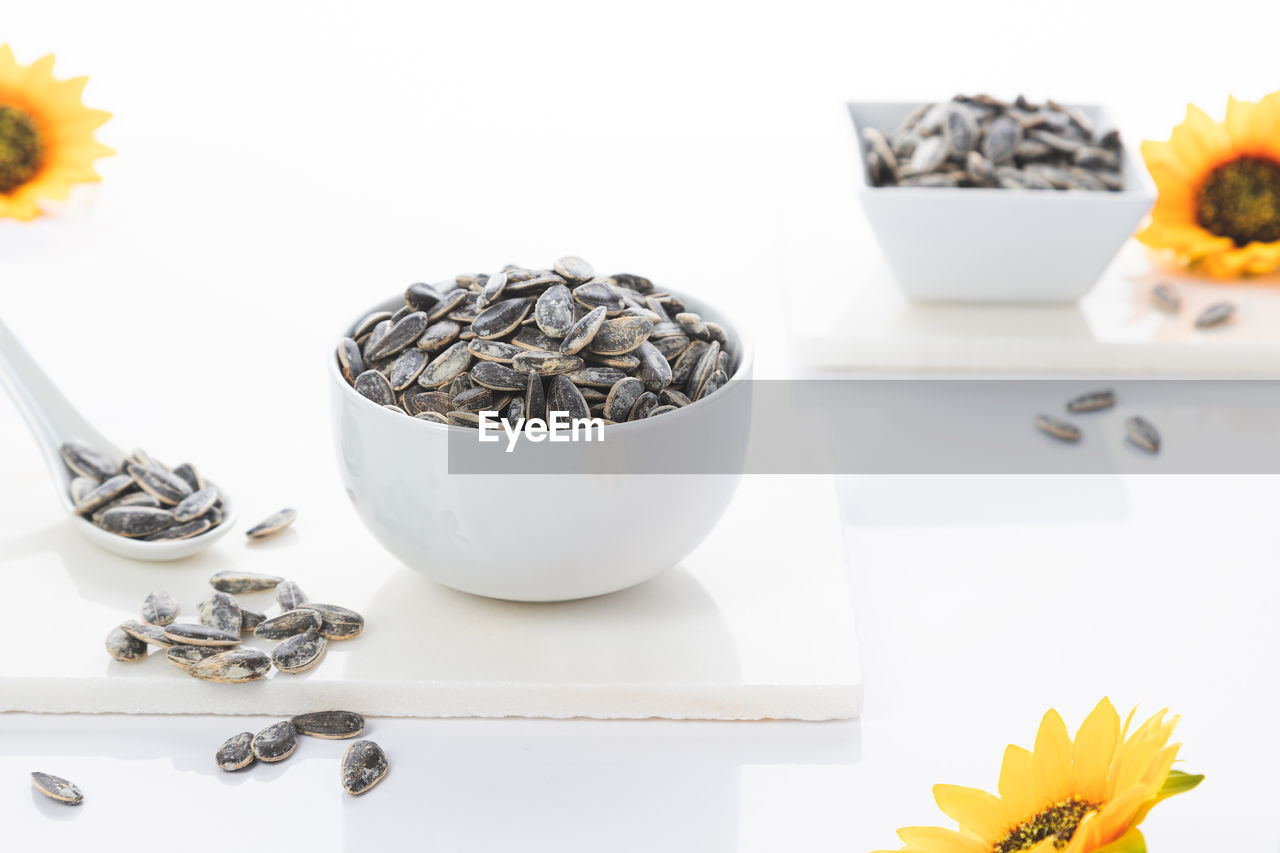 Two bowls of sunflower seeds with sunflowers on white background. selective focus.