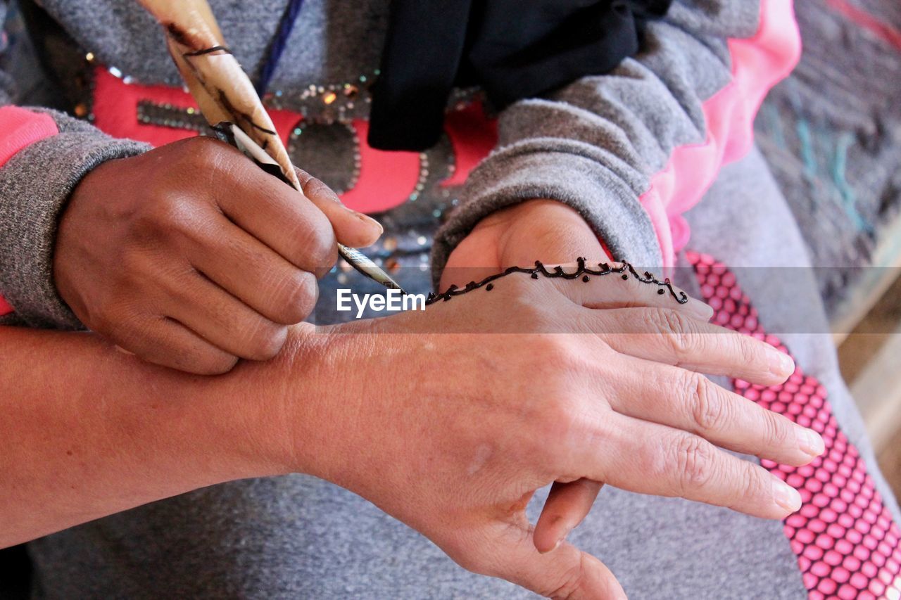 Midsection of artist making henna tattoo on hand of woman