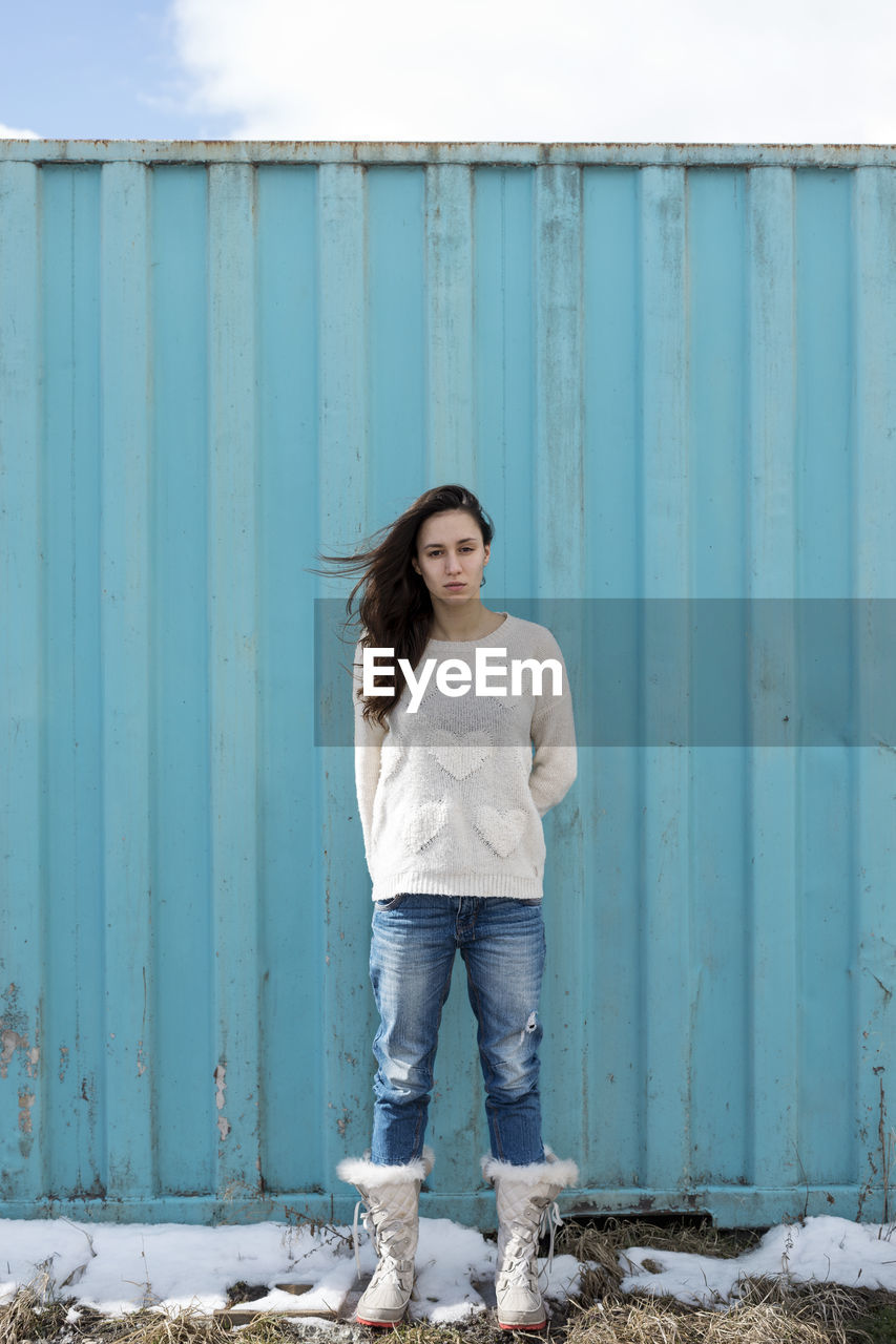 Portrait of woman standing against blue metallic container