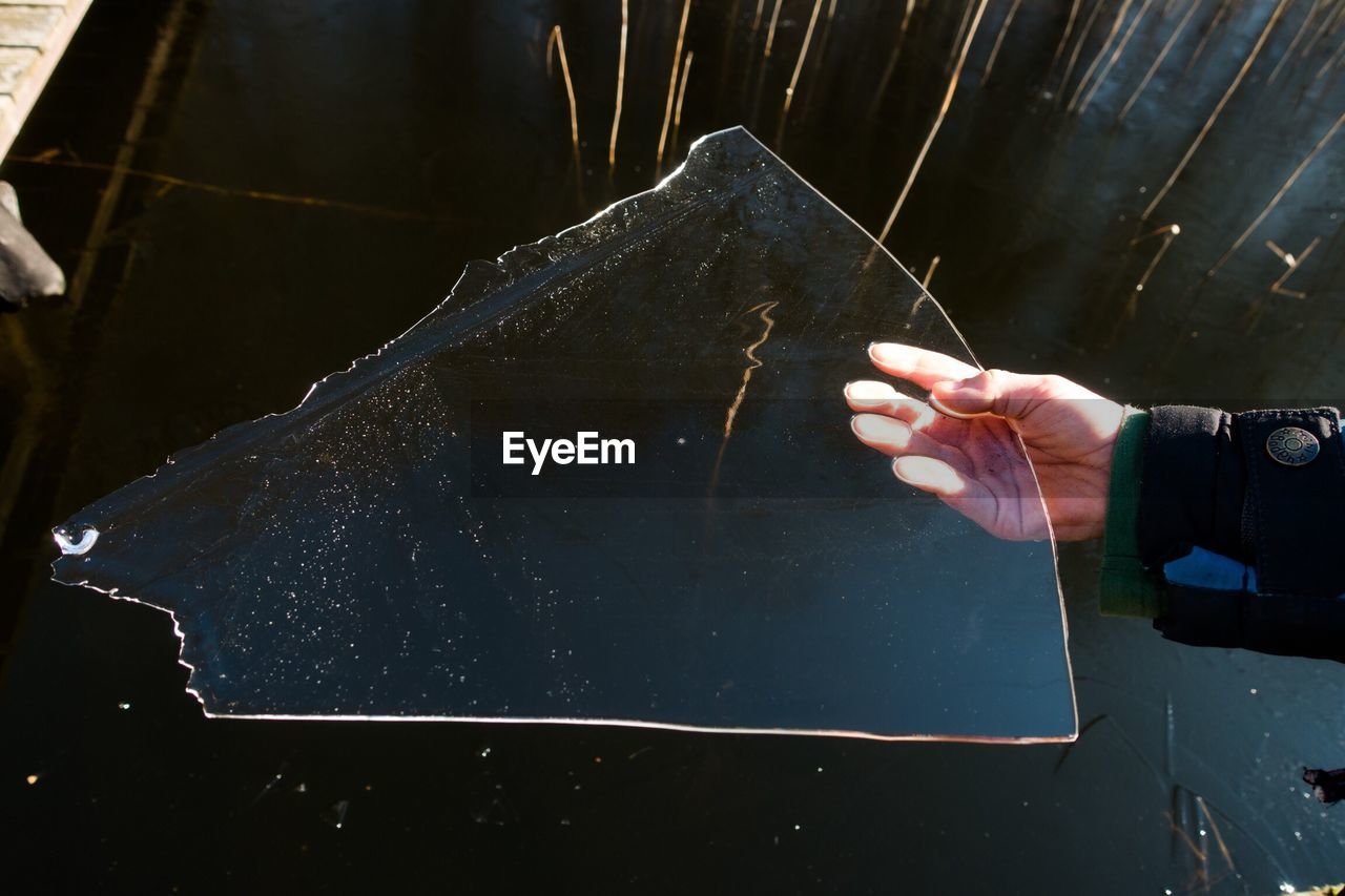 Cropped image of person holding frozen ice over lake