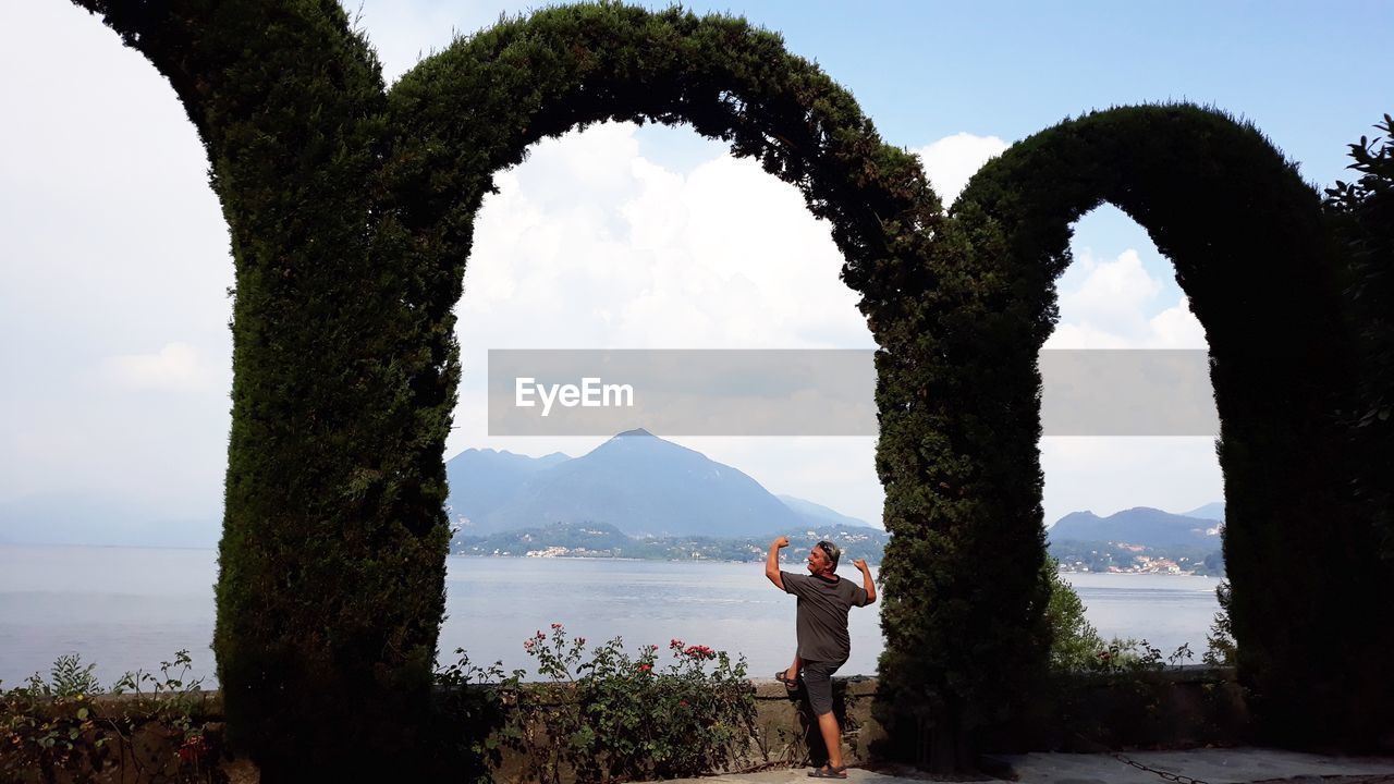 Man standing by arch made with creeper plants against sea and sky