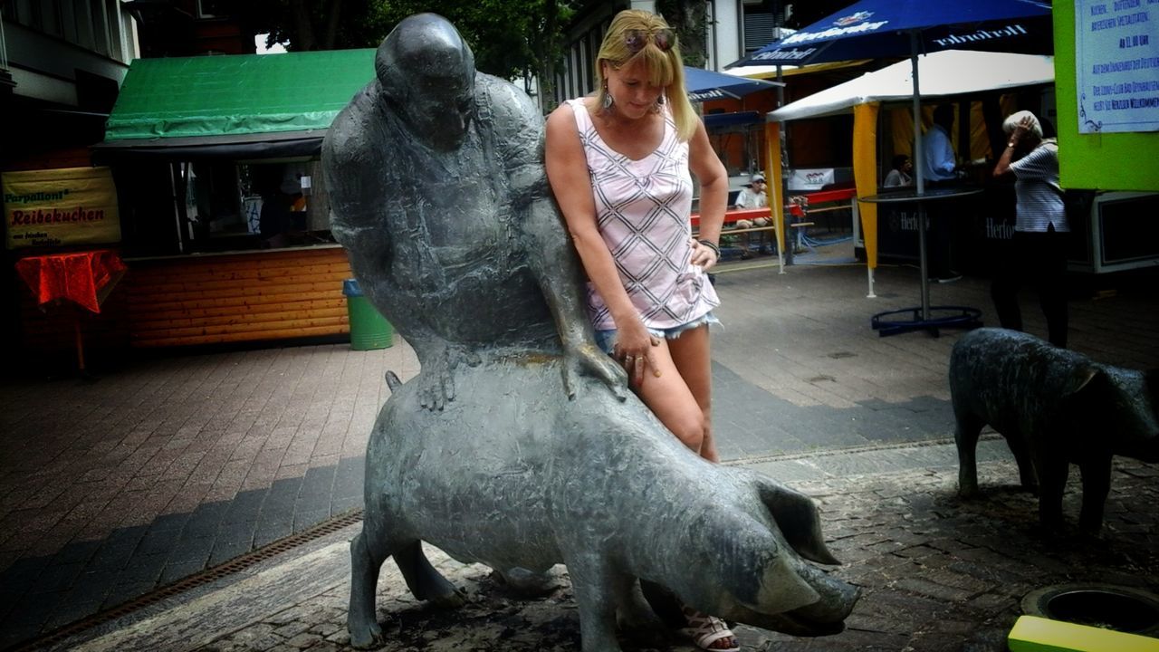 Full length of mid adult woman standing by statues on street in city