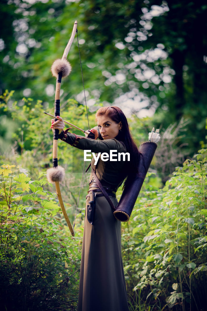 Beautiful woman holding bow and arrow standing outdoors
