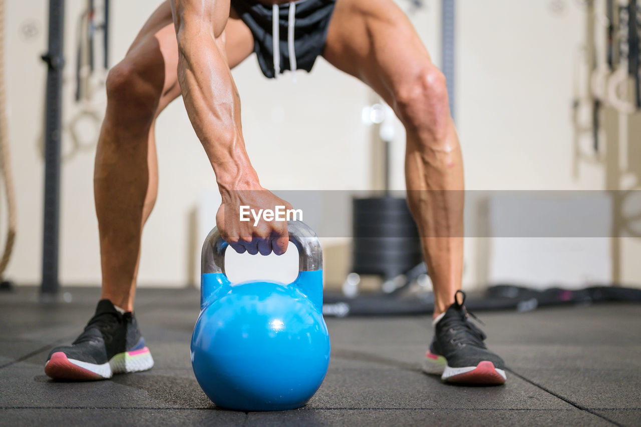 Low section of man holding kettlebell on floor in gym