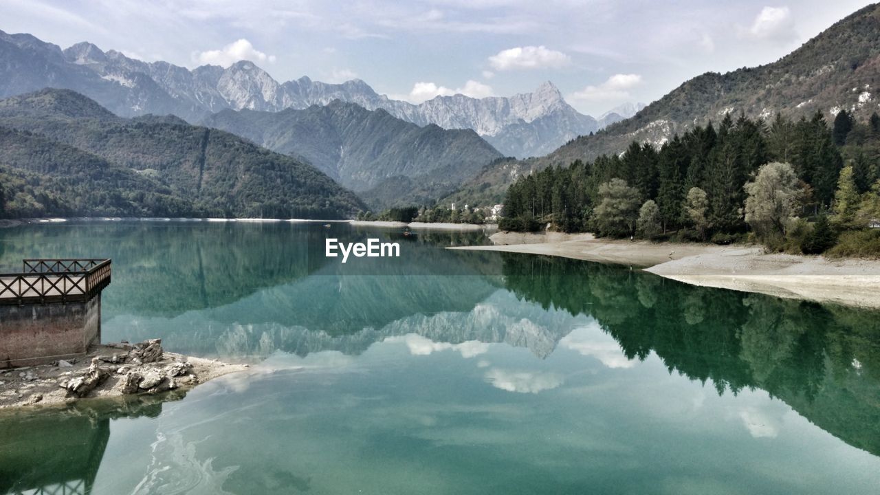 Scenic view of lake by mountains with reflection against cloudy sky