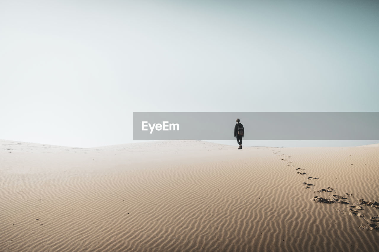 Person walking on desert against clear sky