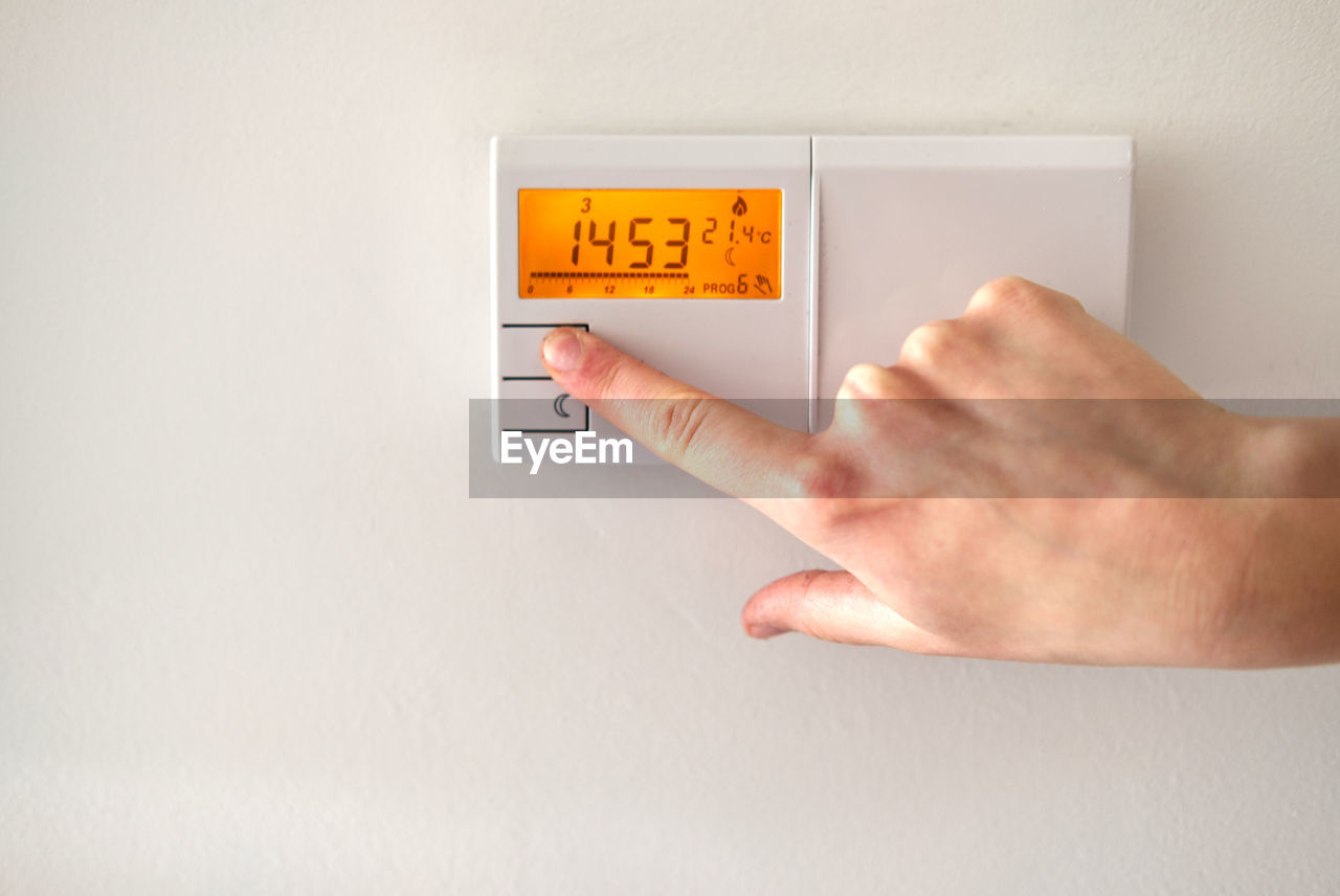 Young woman's hand operating electronic thermostat to adjust temperature at home