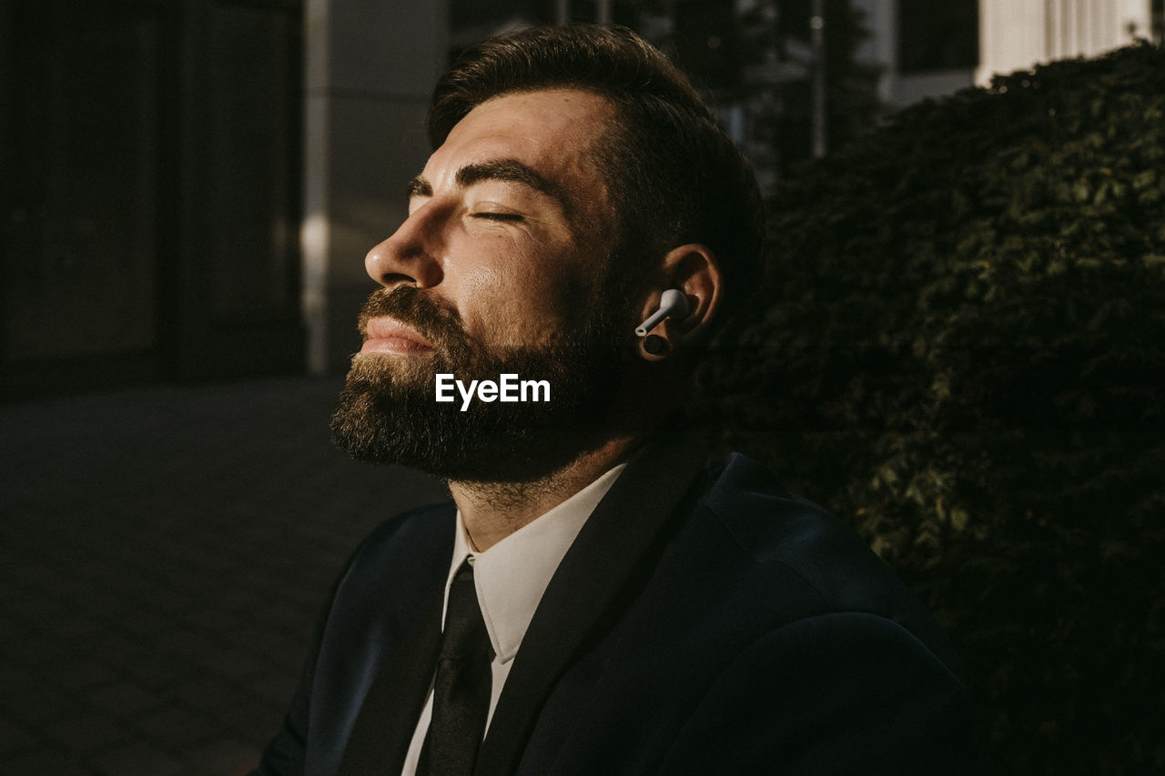 Businessman with eyes closed listening music through wireless earphones