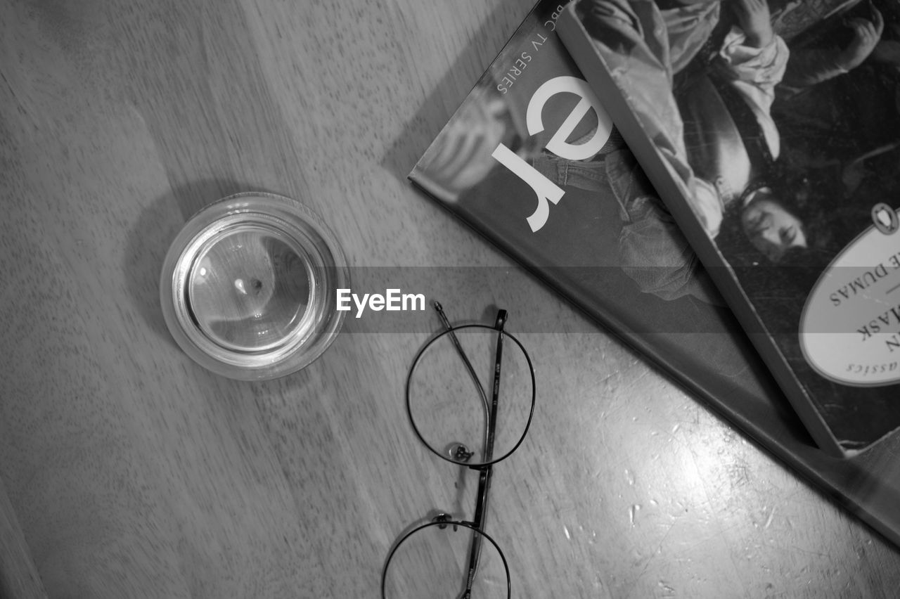 Directly above shot of water in glass by books and eyeglasses on table