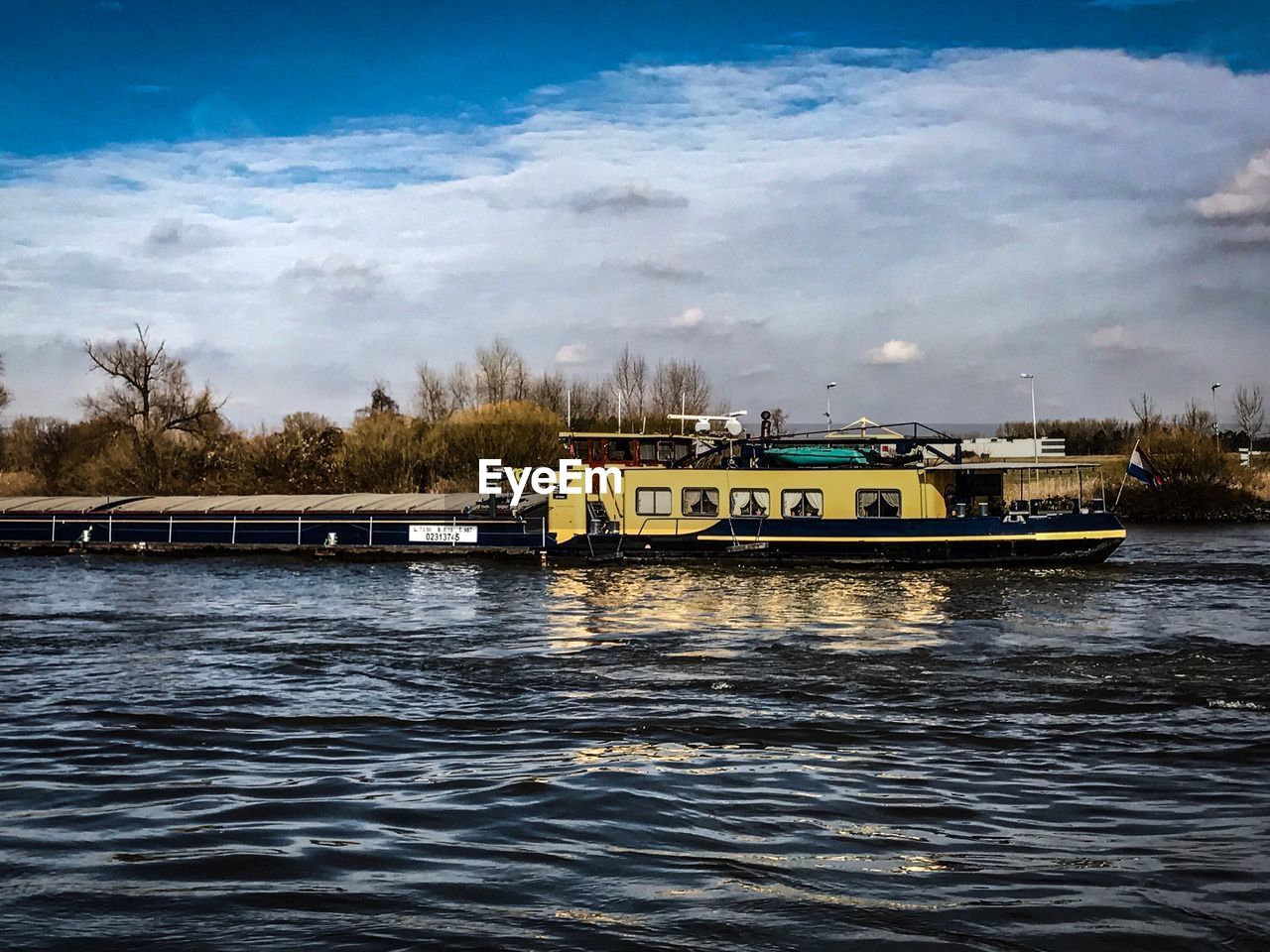 BOATS ON TREE BY RIVER AGAINST SKY