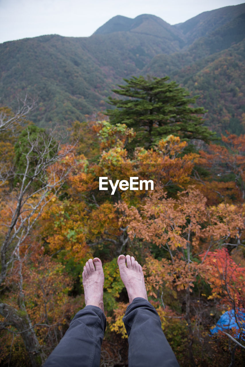 Low section of person sitting on mountain against sky