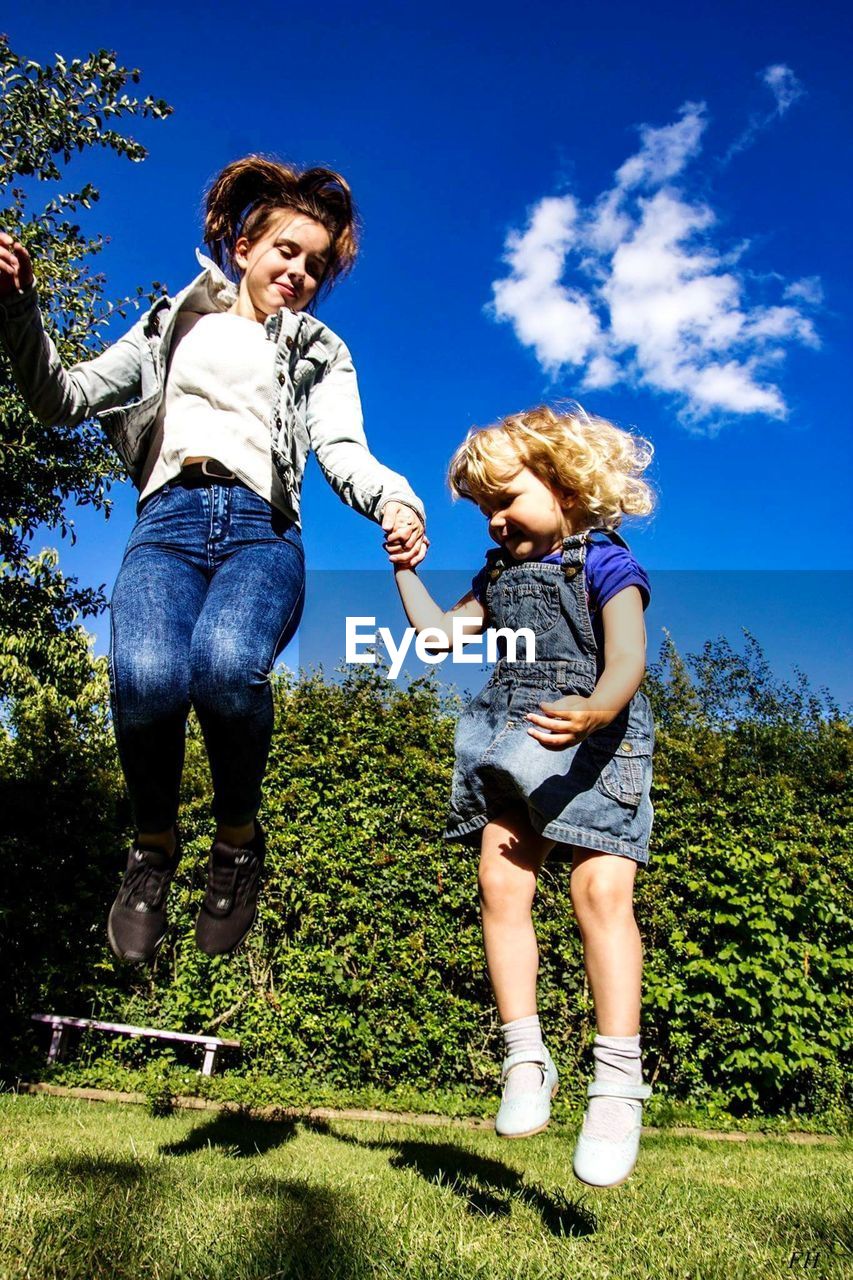 Siblings holding hands while jumping on field against sky