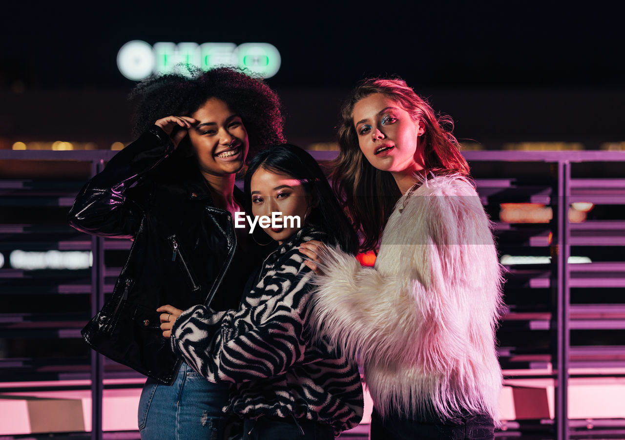 Portrait of smiling women standing by railing outdoors at night