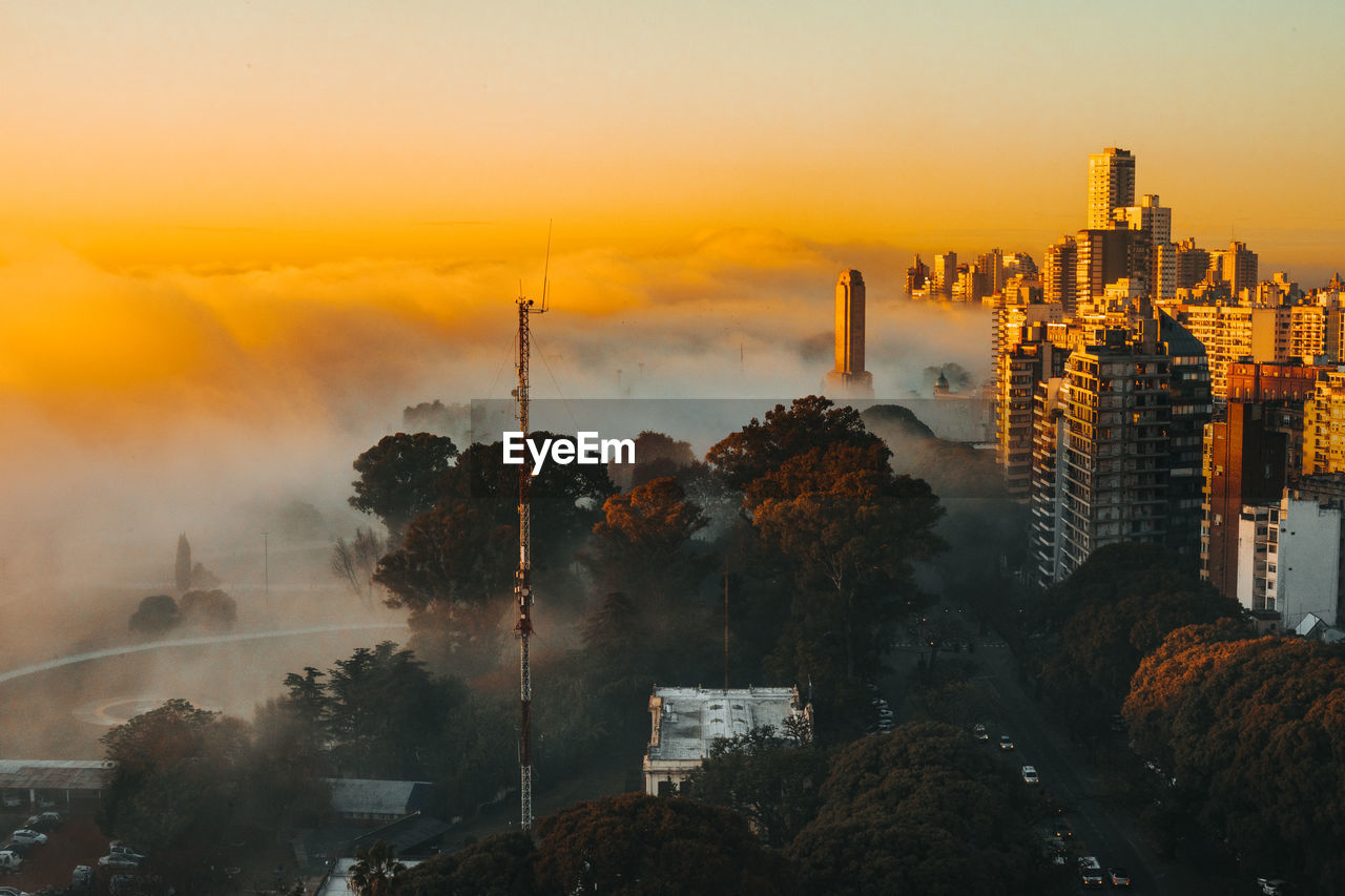 Trees and buildings against sky during sunset