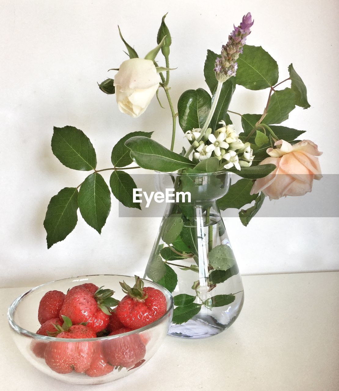 Close-up of strawberries in bowl with white flowers vase on table