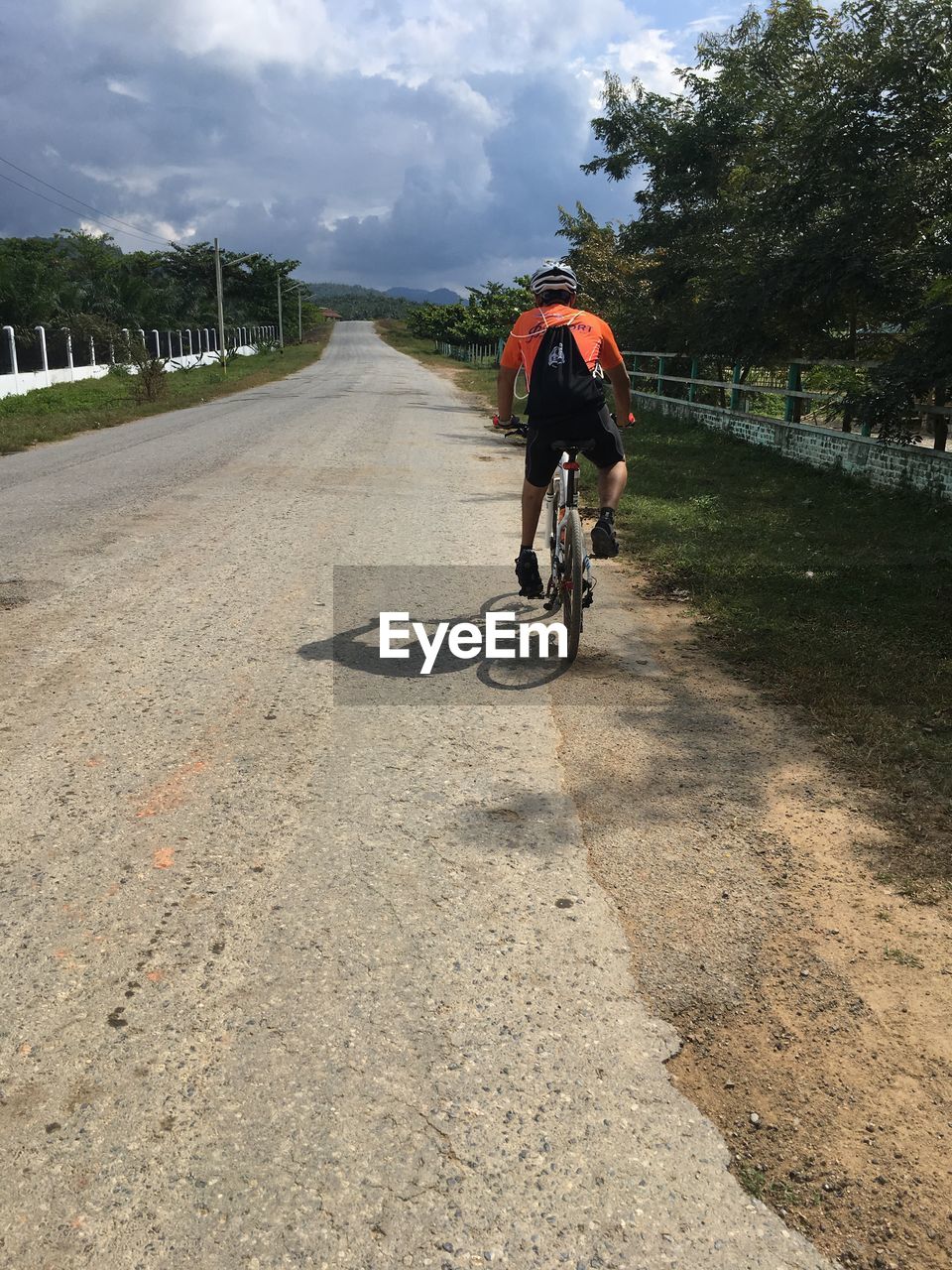 MAN RIDING BICYCLE ON ROAD AGAINST SKY