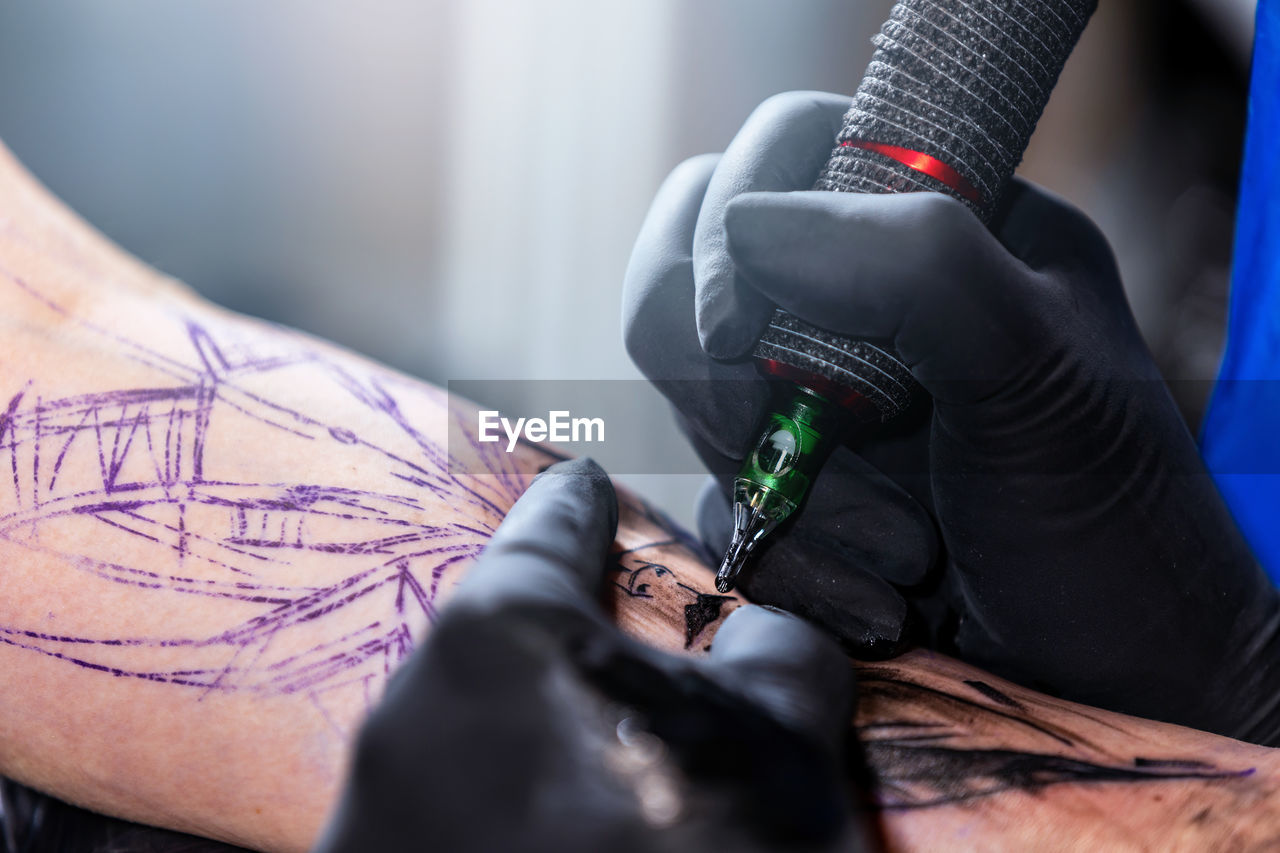 adult, hand, indoors, occupation, arm, skill, tattoo, men, creativity, tattooing, one person, working, limb, protective workwear, human limb, protection, protective glove, holding, close-up, accuracy, selective focus, blue, young adult, expertise