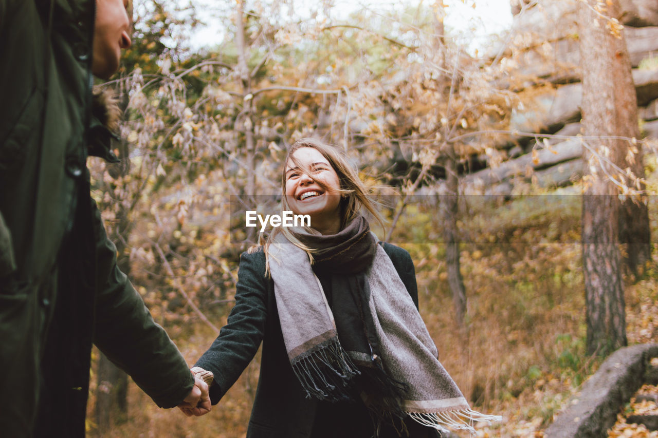 Smiling young woman holding hands while standing against trees