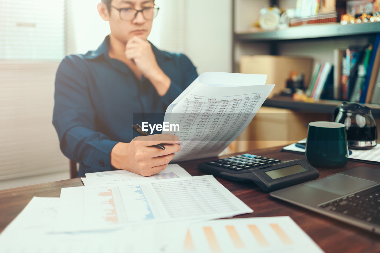 Midsection of man holding paper while sitting on table