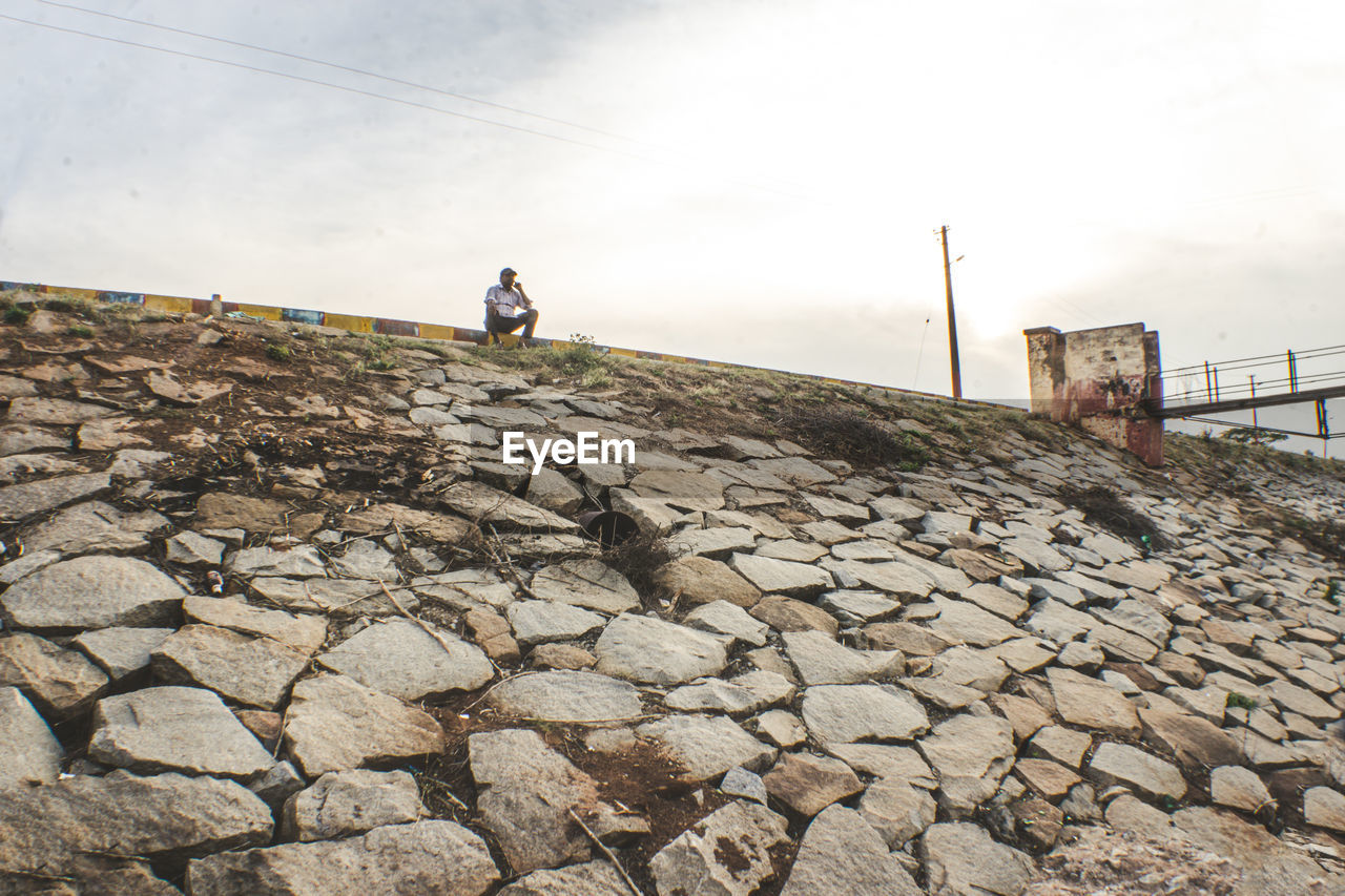 Man sitting on land against sky