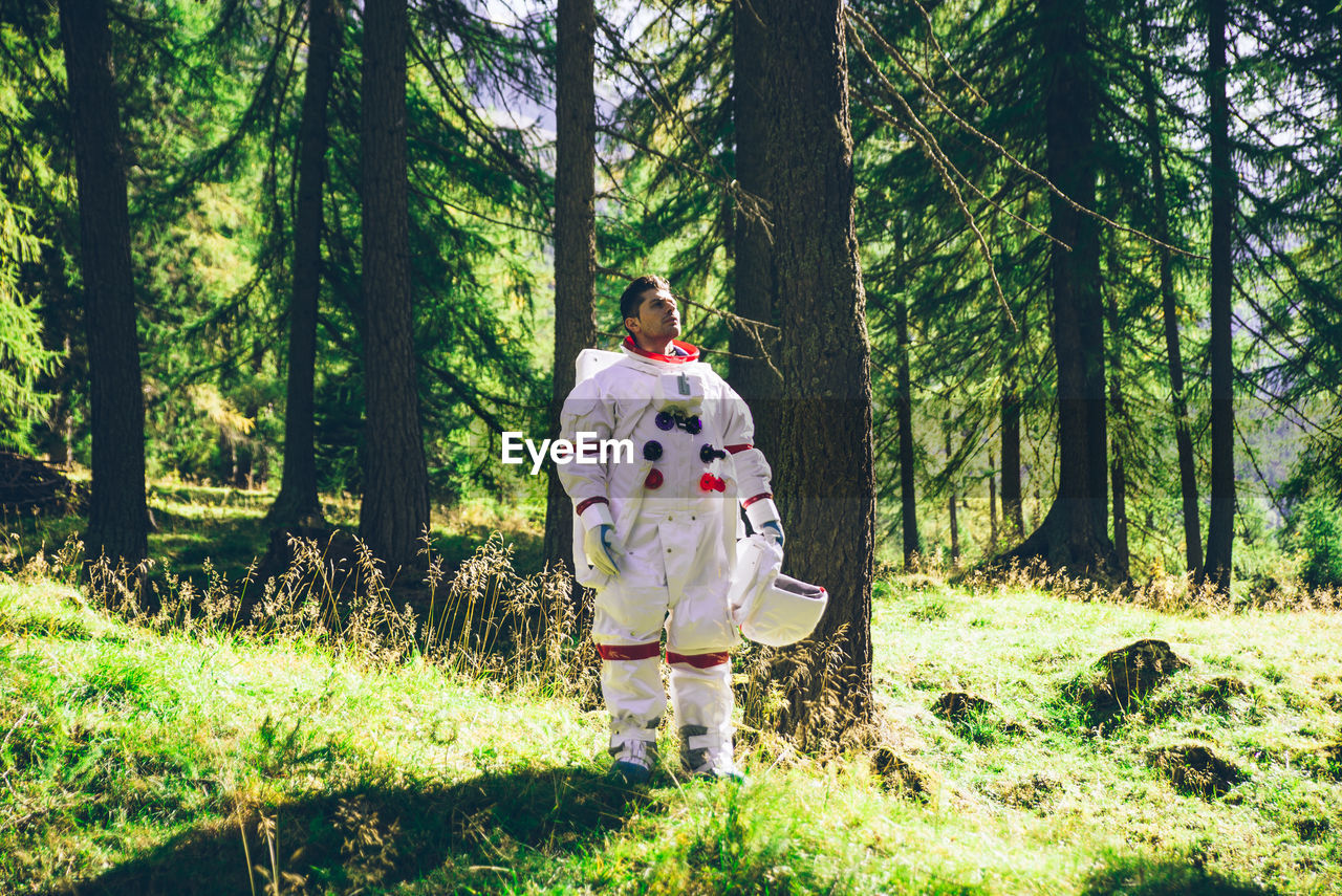 Man standing by tree trunk in forest