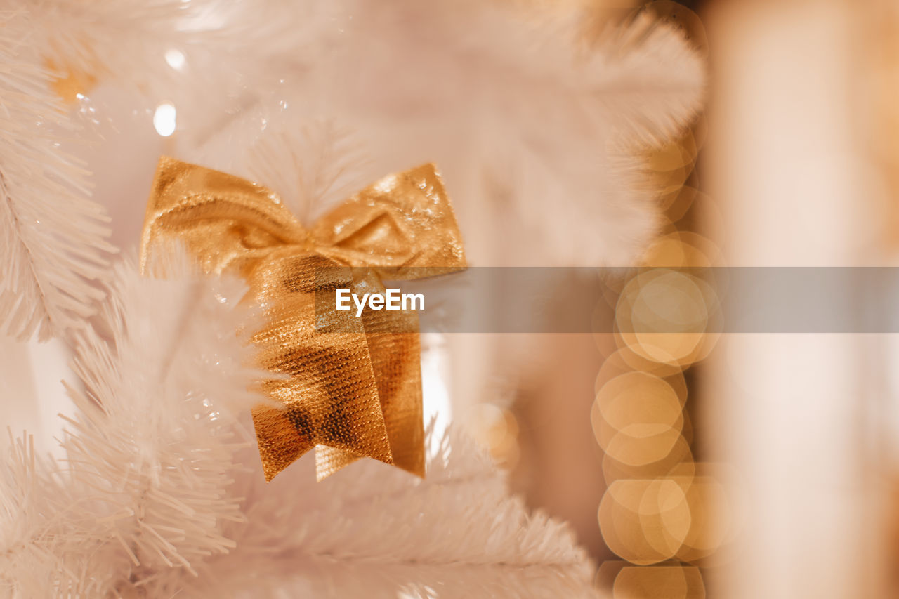 Golden christmas bow hanging on the white christmas tree. magic details with bokeh lights