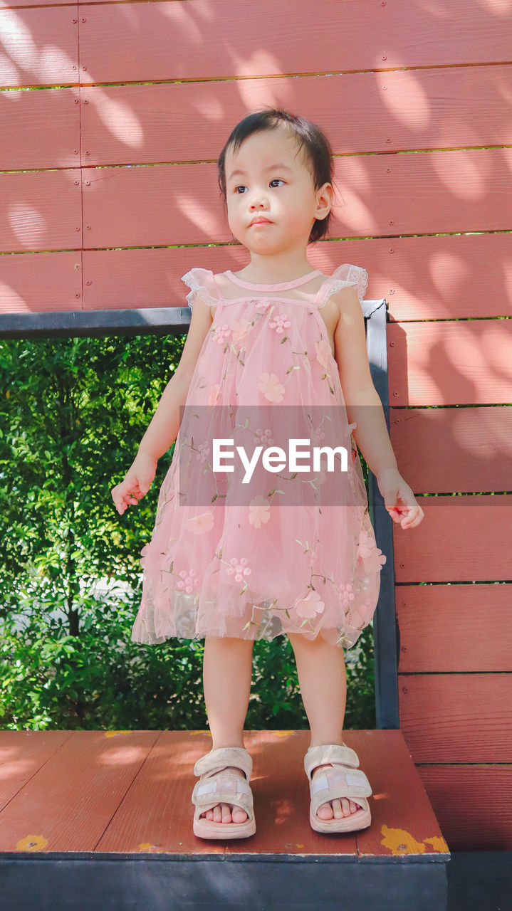 Lovely adorable charming asian little girl is looking down. she is wearing light pink dress.