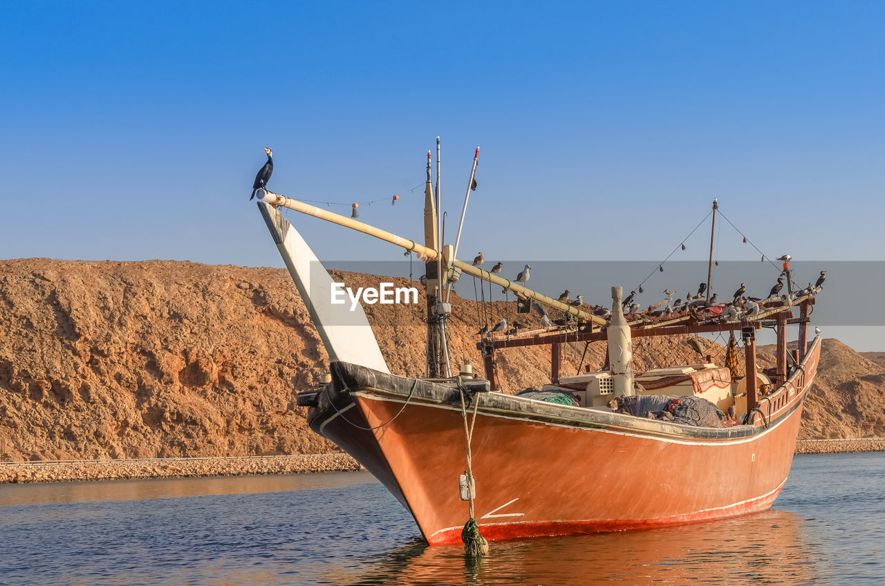 Fishing boat in sea against clear blue sky