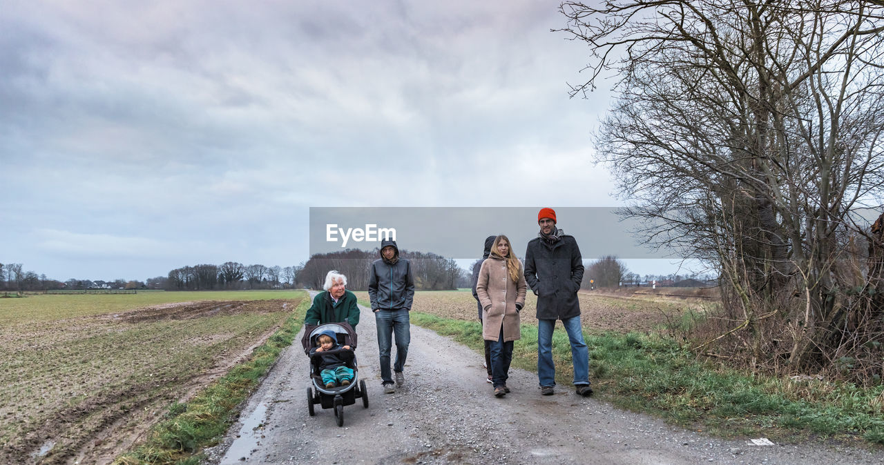 Family on road amidst field against sky