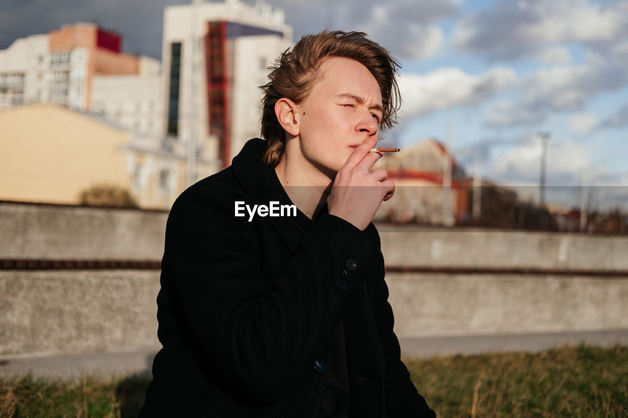 Young man smoking cigarette while sitting outdoors